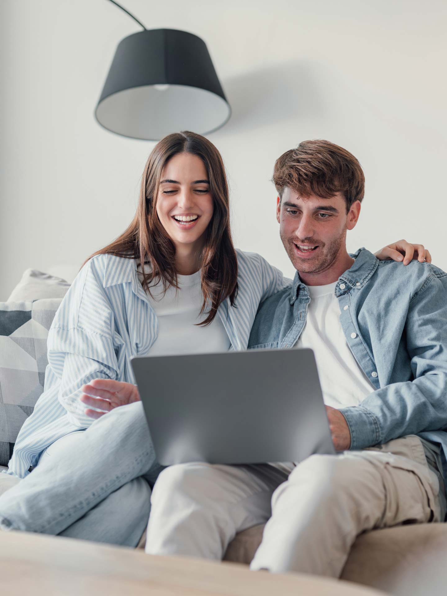 Zwei Personen sitzen nebeneinander auf der Couch und haben einen Laptop auf dem Schoss